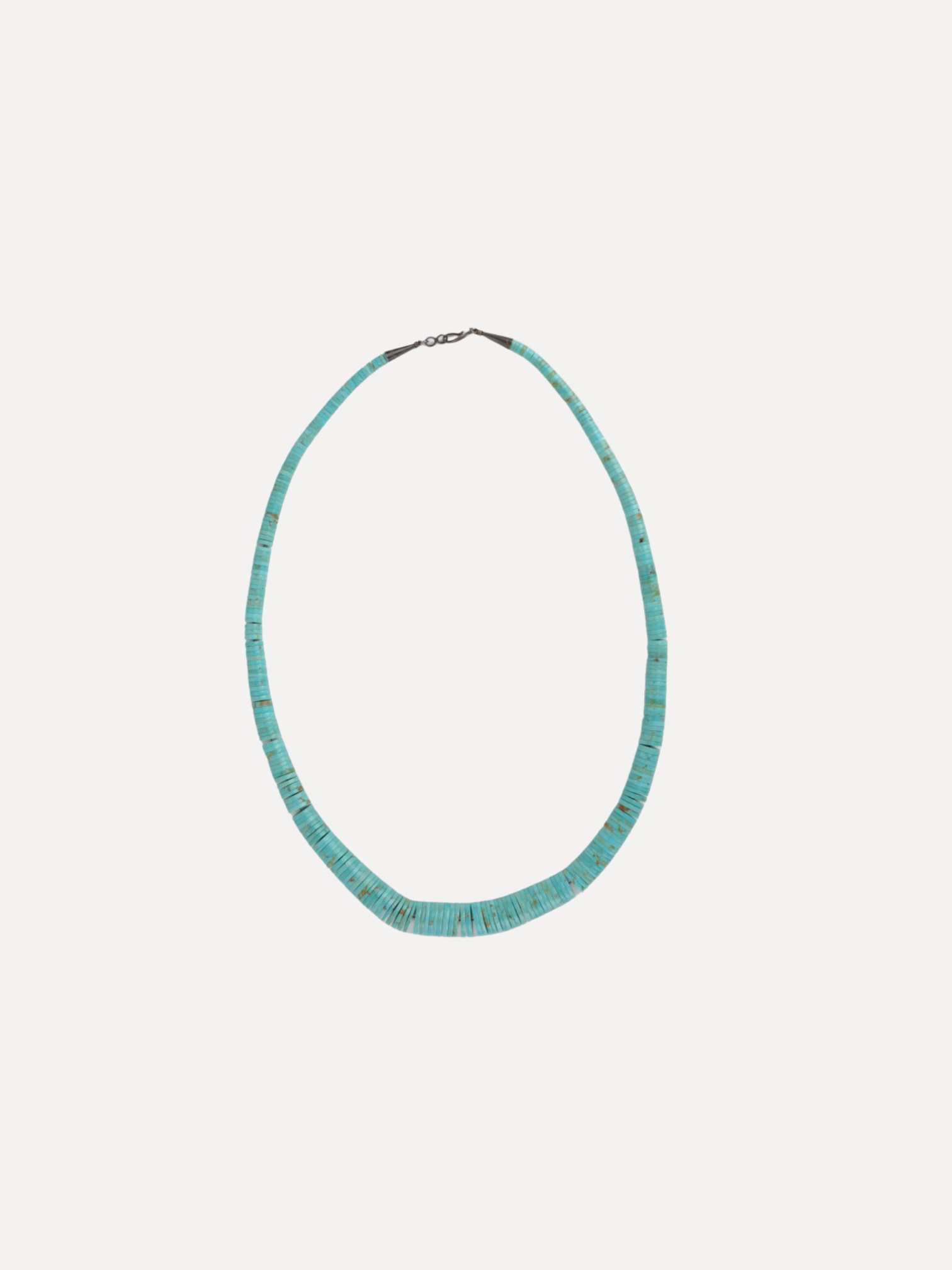 A beaded necklace made of small turquoise-blue beads with a silver-toned clasp, displayed against a solid off-white background.