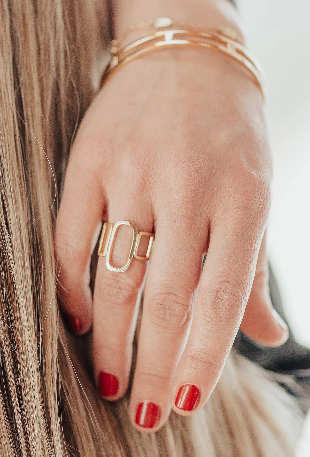 Hand wearing a gold ring with red nail polish on a blurred background