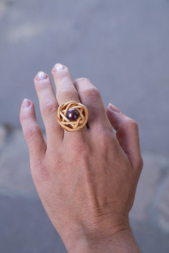 Hand wearing a gold ring with a central pearl against a blurred background. Bamboo ring with black pearl ring