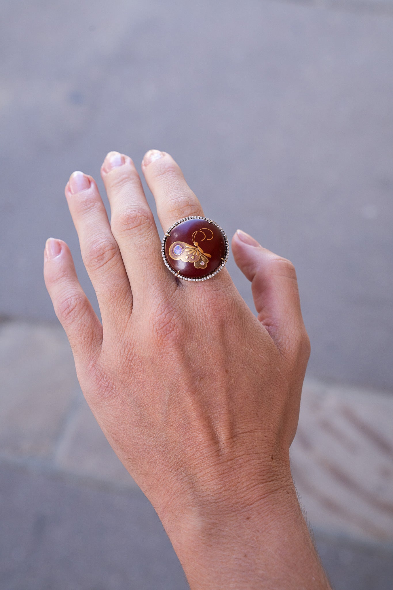 Hand wearing a ring with a decorative design on a blurred background. Butterfly Ring