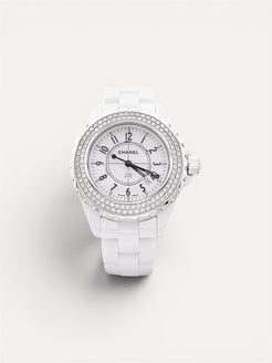Chanel watch with white strap and diamond-studded face on a light gray background
