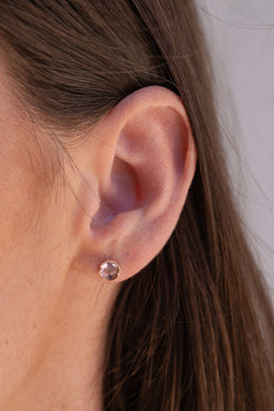 Close-up of an ear wearing a rose gold earring with a clear gemstone. Irene Neuwirth Rose De France Studs