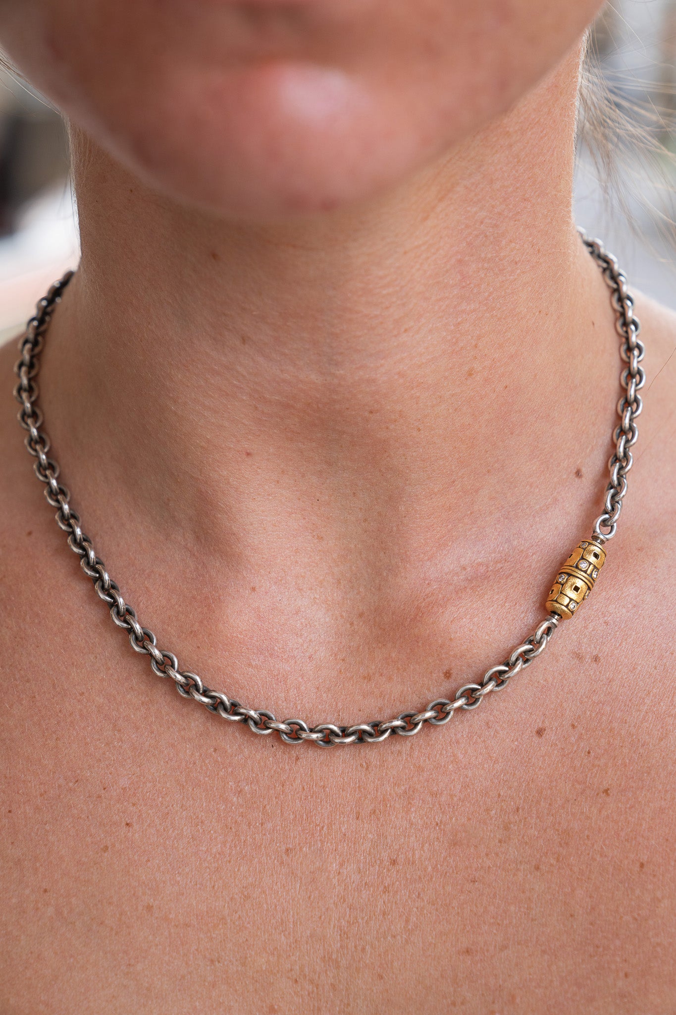 Close-up of a person wearing a chain necklace with a gold bead.