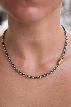 Close-up of a person wearing a chain necklace with a gold bead.