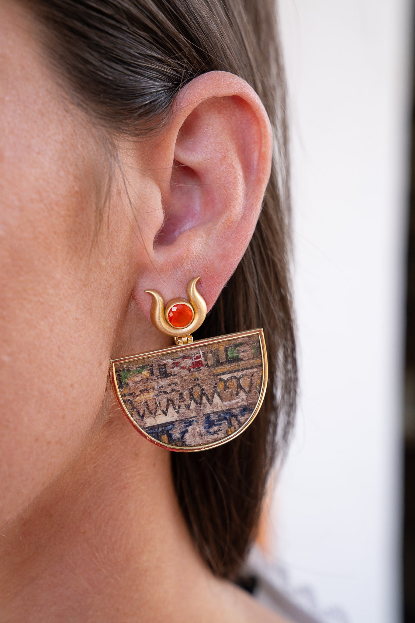Close-up of an ear wearing a decorative earring with a red gemstone. Egypt Earrings Silvia Furmonavich