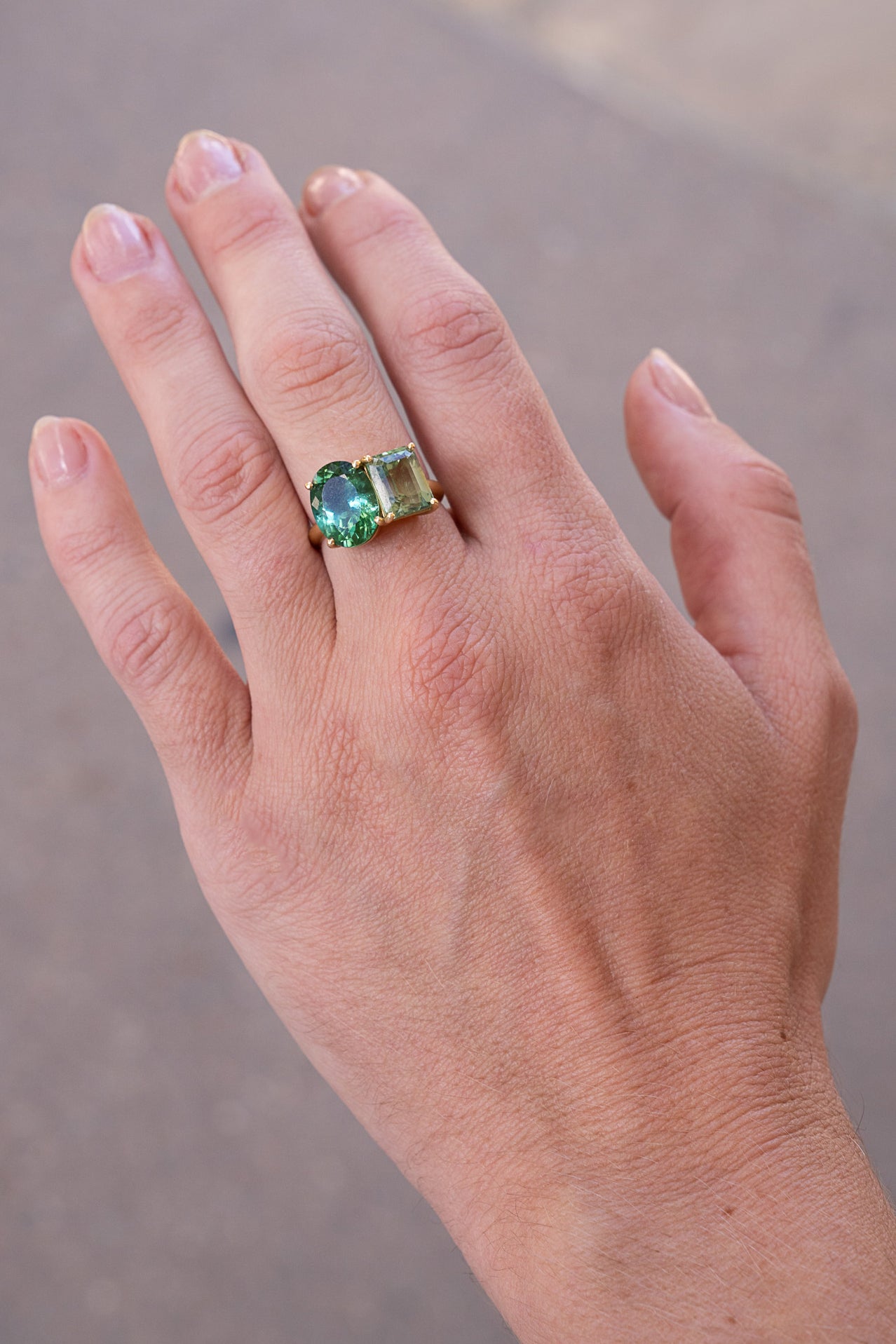 Hand wearing a ring with two green gemstones on a neutral background. Gemma-Gem-One-of-a-Kind-Green-Tourmaline-Ring-Irene-Neuwirth