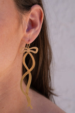 Gold bow-shaped earring worn by a person with a neutral background. Gold-Classic-Ribbon-Earrings-Irene-Neuwirth-510416751