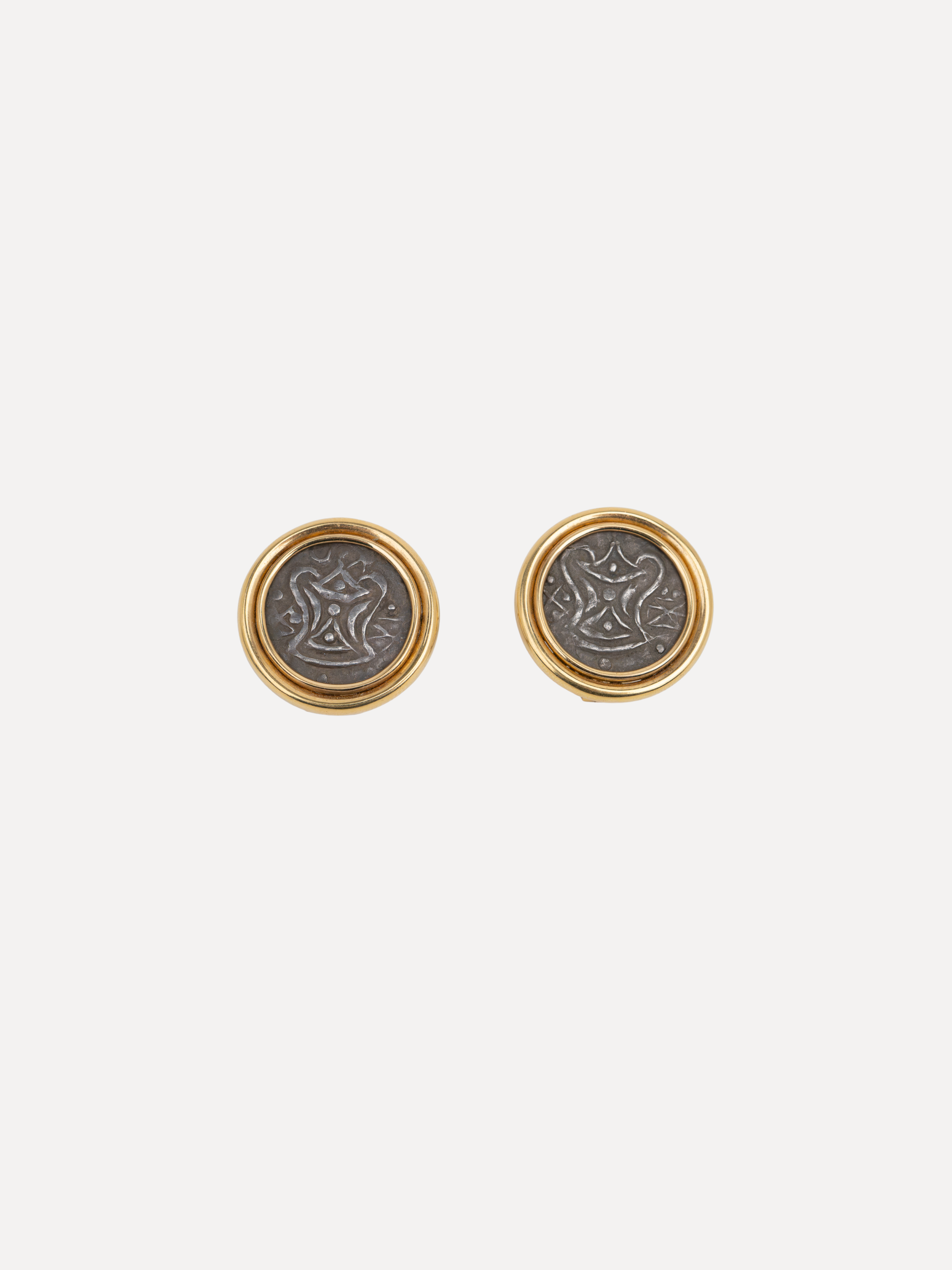 A pair of gold and silver stud earrings with circular coin-like designs, displayed on a light gray background.