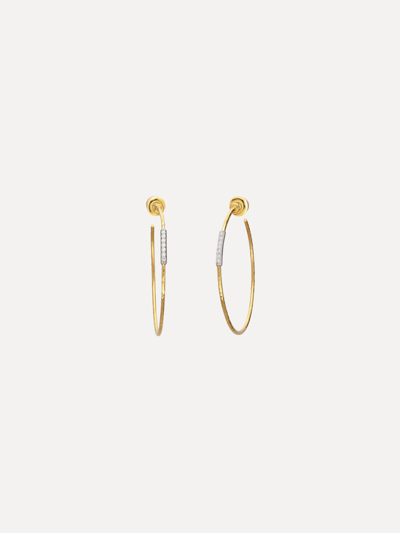 Gold hoop earrings with embedded stones on a light beige background