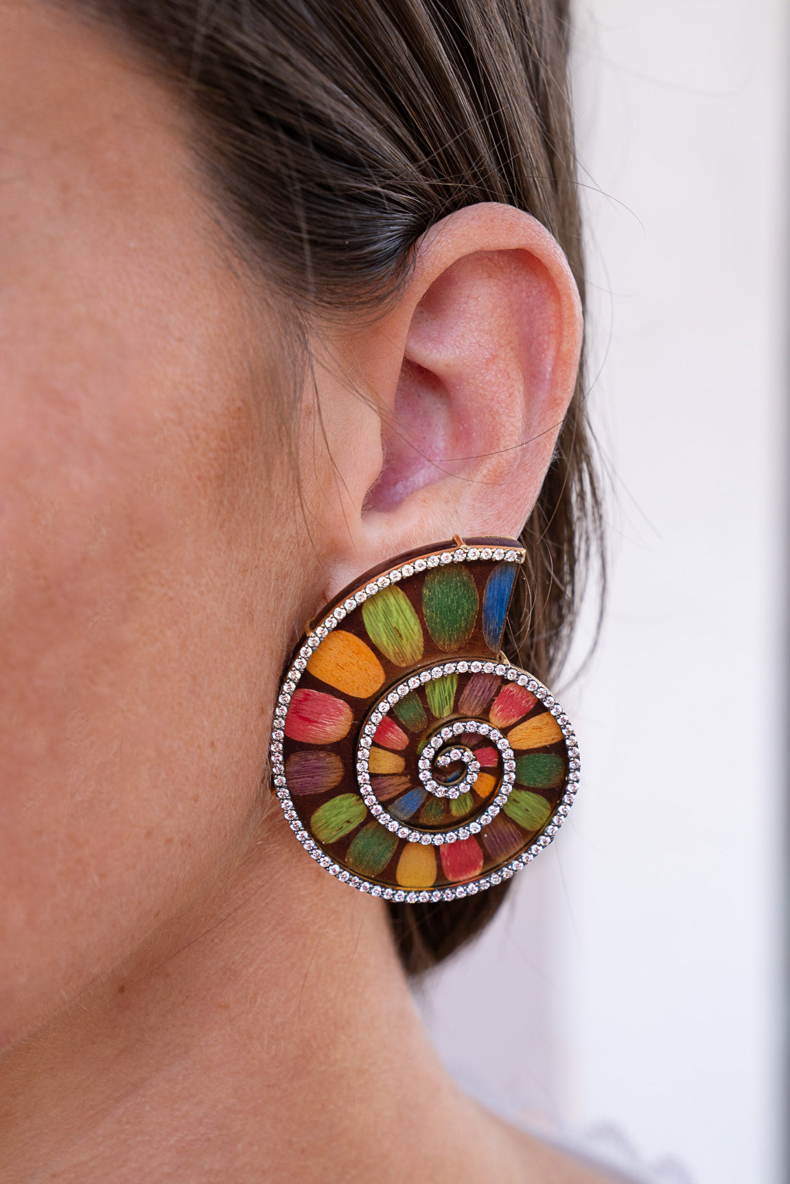 Close-up of a colorful spiral earring on an ear with a white background. Marquetry-Shell-Pattern-Earrings-with-Diamonds-Silvia-Furmanovich