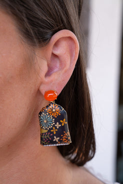 Close-up of an ear wearing a colorful floral earring with an orange center. Marquetry earrings with orange sapphire and carnelian