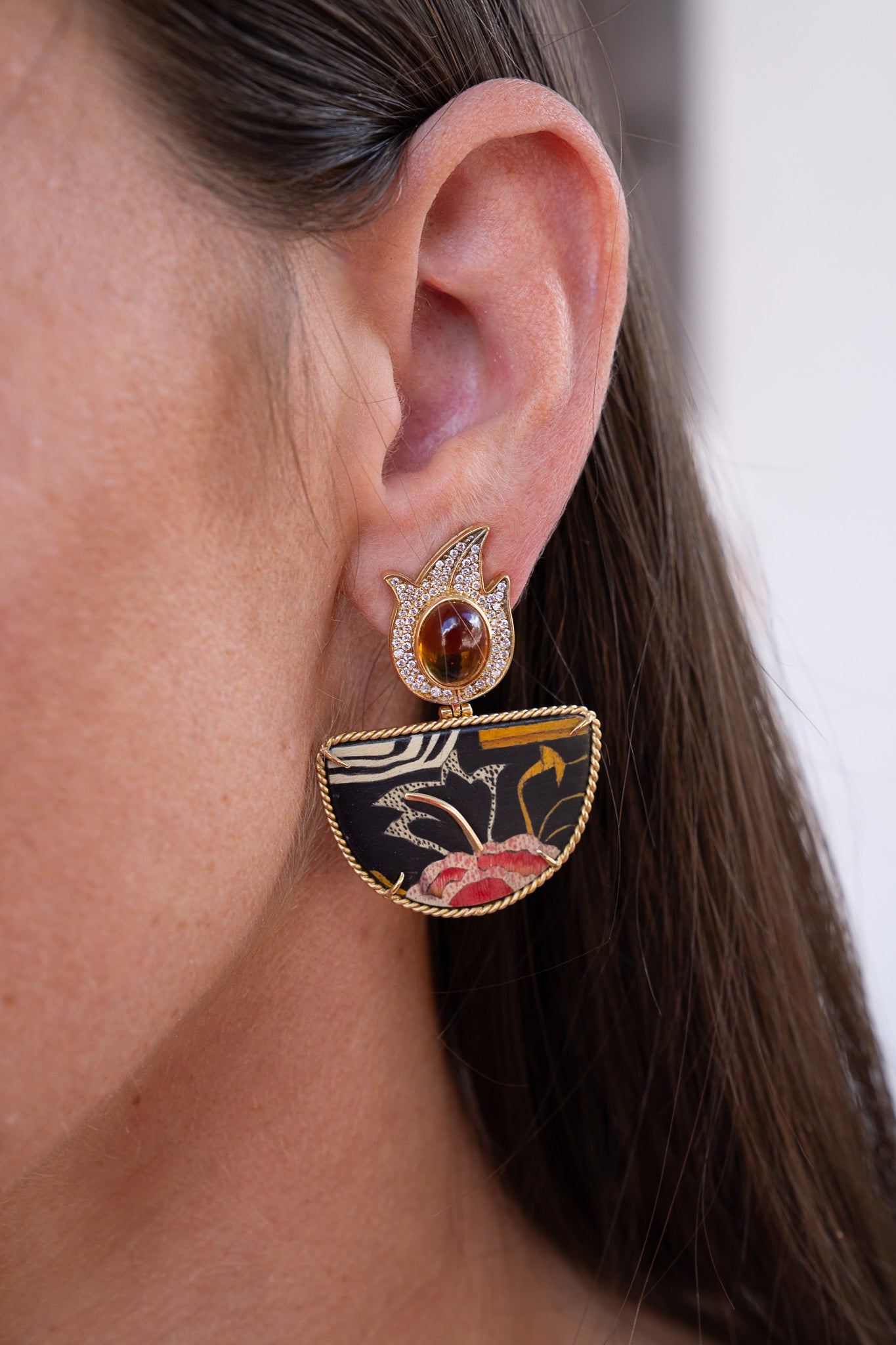 Close-up of a woman wearing an ornate earring with a dark background. Marquetry earrings with halfmoon format