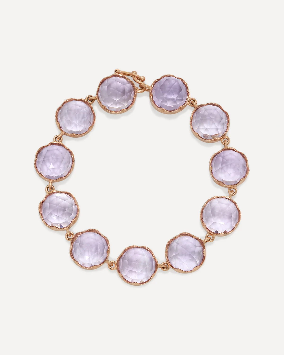 A gold-tone bracelet featuring round, faceted light purple gemstones, arranged in a circle on a light off-white background.