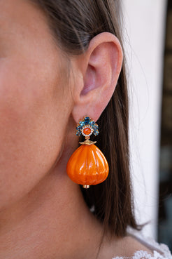 Close-up of an orange earring with a blue and gold center worn by a person. Orange lacquered marquetry earrings