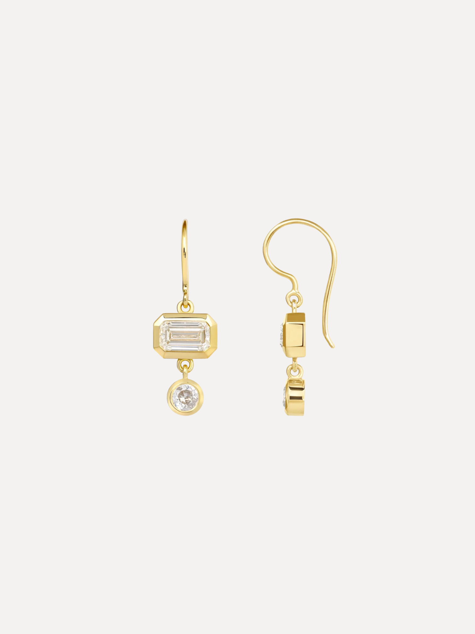 A pair of gold drop earrings on a light gray background. One earring features a rectangular baguette-cut clear gemstone in a gold bezel setting, and the other shows the side profile with a small round clear gemstone below a gold connector.