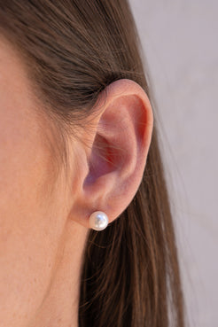 Close-up of an ear wearing a pearl stud earring with a neutral background. Akoya Pearl, Irene Neuwirth