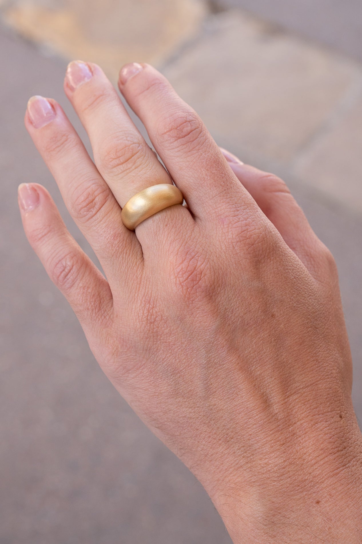 Hand wearing a gold ring with a blurred background. Puffed-Gold-Dome-Ring-Irene-Neuwirth