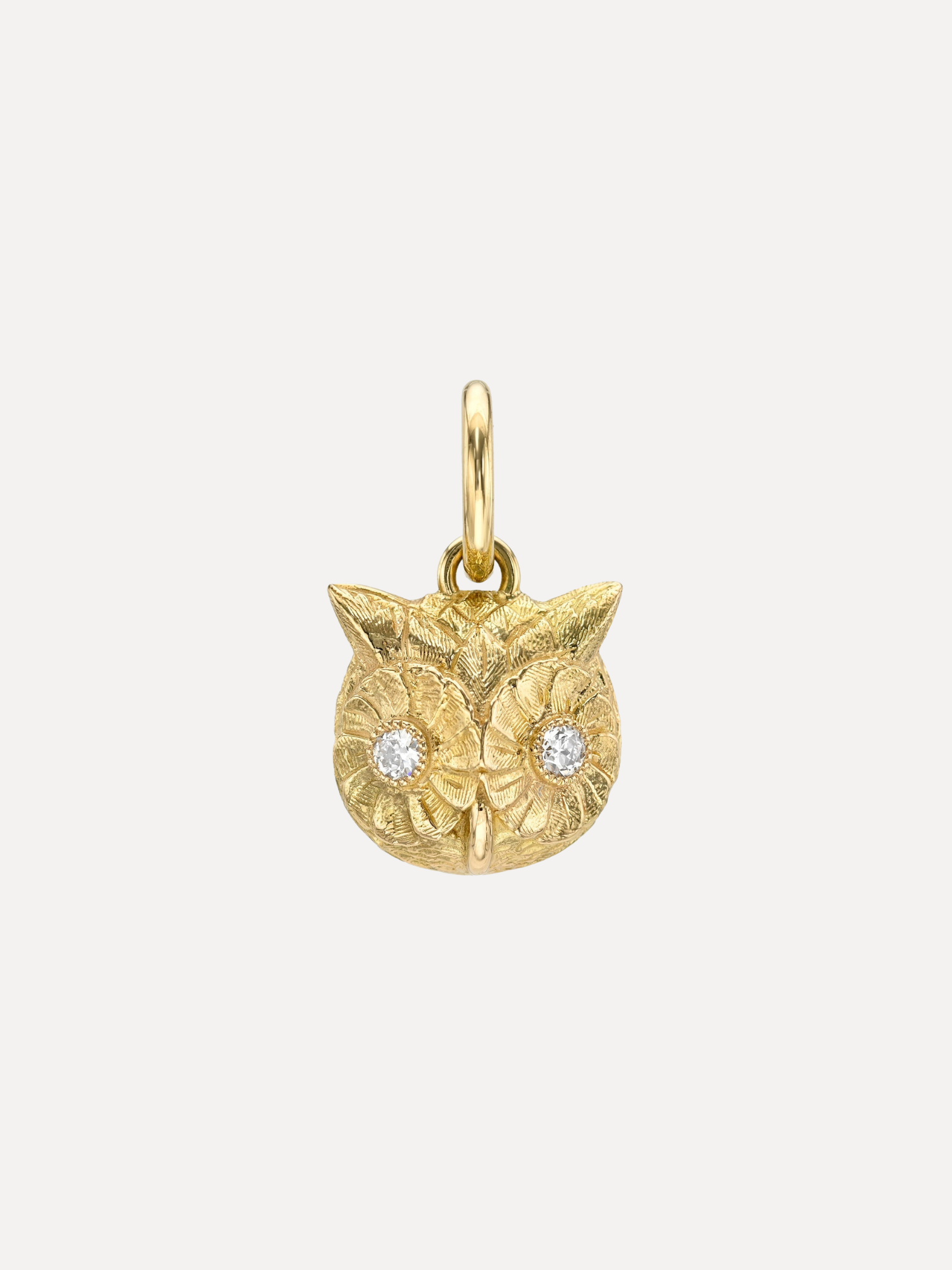 A gold owl-shaped pendant with textured detailing and two clear gemstone eyes, shown on a light gray background.