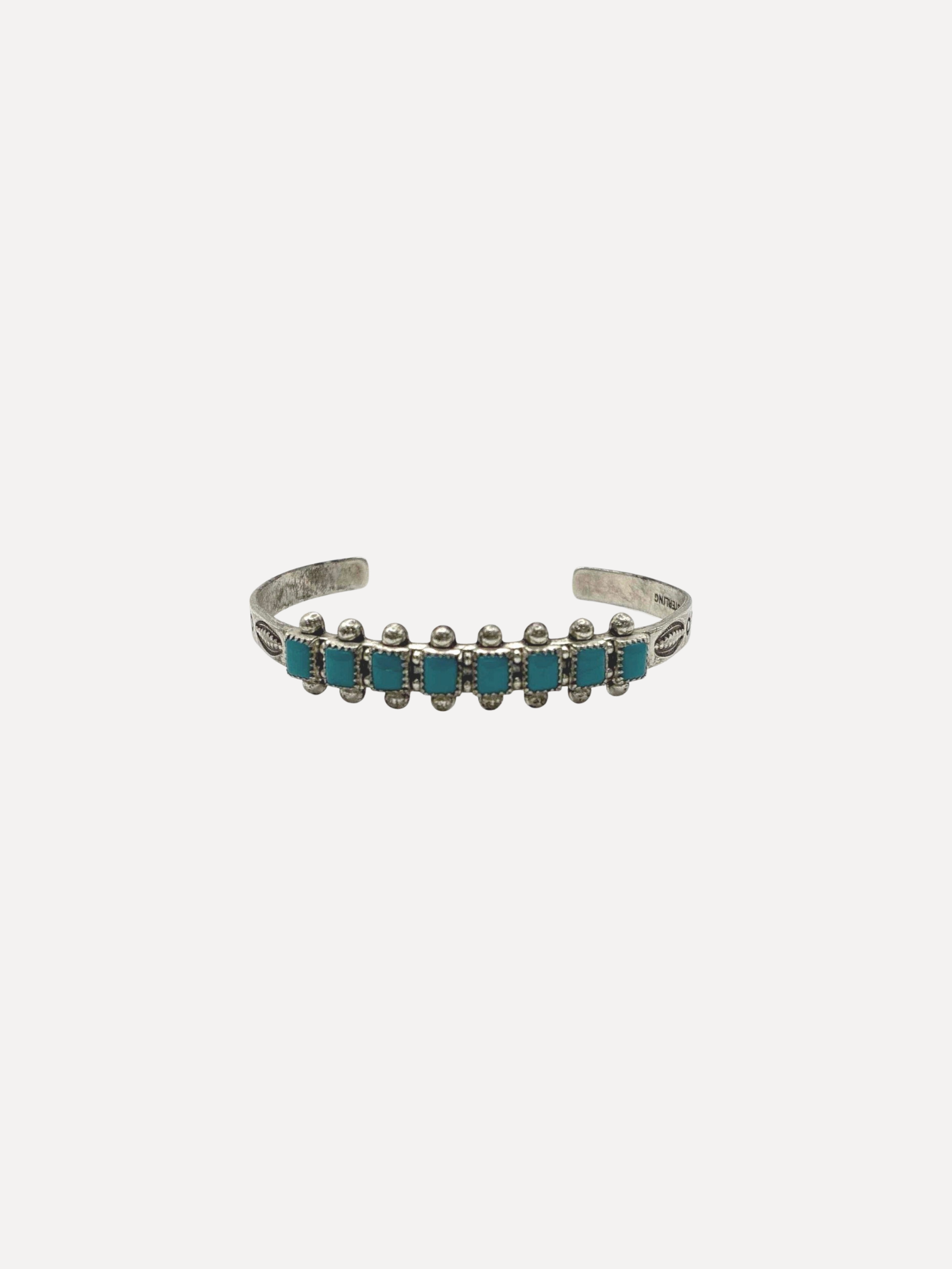A silver cuff bracelet featuring a row of small turquoise blue rectangular stones set in silver bezel settings, shown against a plain light gray background.