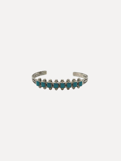 A silver cuff bracelet featuring a row of small turquoise blue rectangular stones set in silver bezel settings, shown against a plain light gray background.
