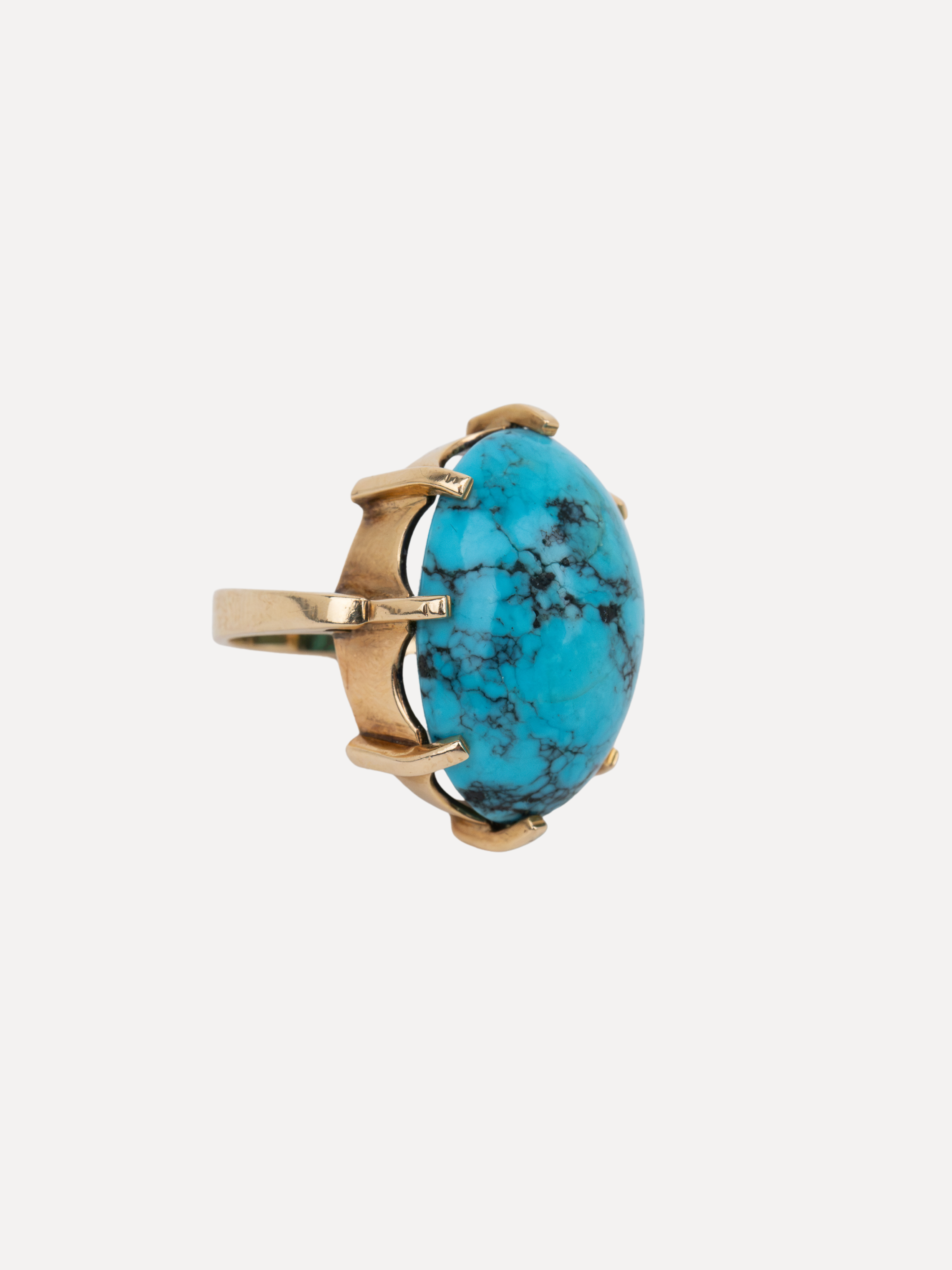 A gold ring featuring a large oval turquoise stone with black veining, set in a claw-style gold prong setting against a light gray background.