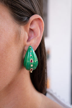 Close-up of a person wearing green teardrop earrings with red gemstones. Turquoise lacquered marquetry earrings