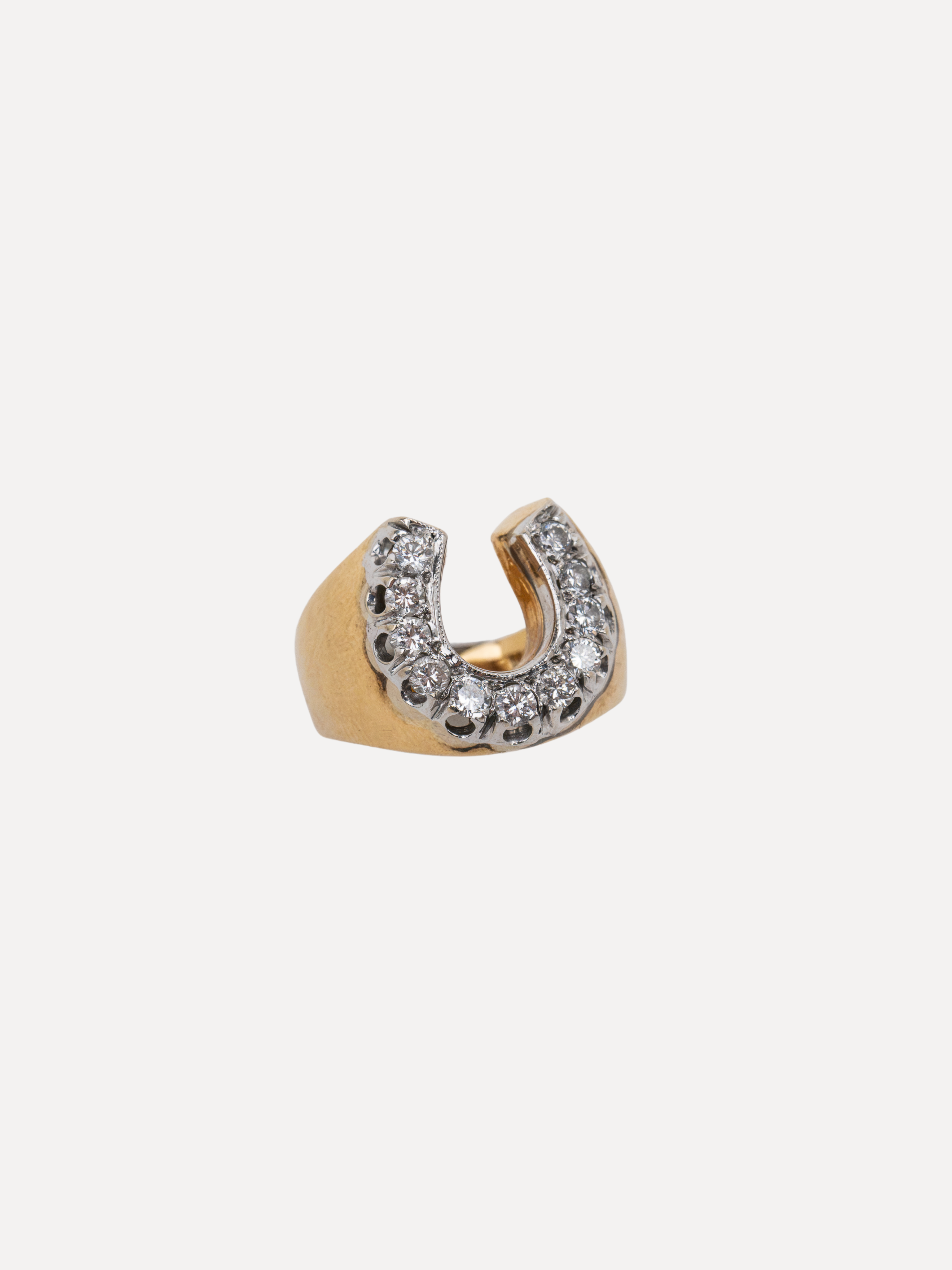 A gold crescent-shaped ring featuring a row of clear pavé-set stones along the outer curve, photographed on a solid off-white background.