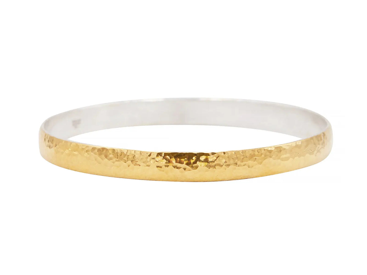 Bangle bracelet in sterling silver plated with 24K gold. It measures 5.8mm wide with rounded edges and is hammered. The diameter is 65mm.  Designed by Gurhan